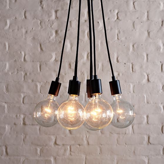 Lampa złożona z żarówek na kablach, na tle bielonej, ceglanej ściany